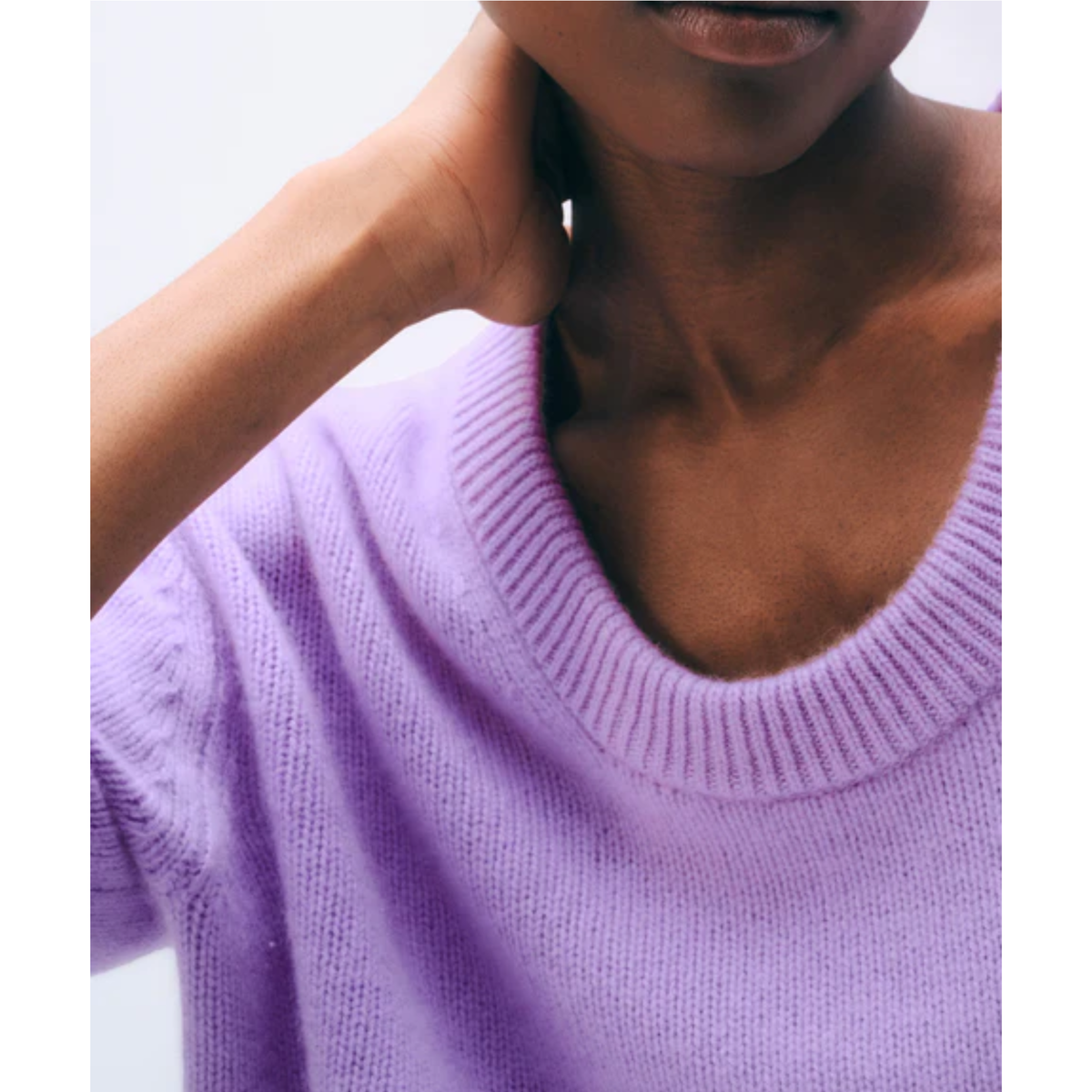 Close-up of a person wearing a soft lavender knit sweater with a wide ribbed crew neckline, against a plain light background.