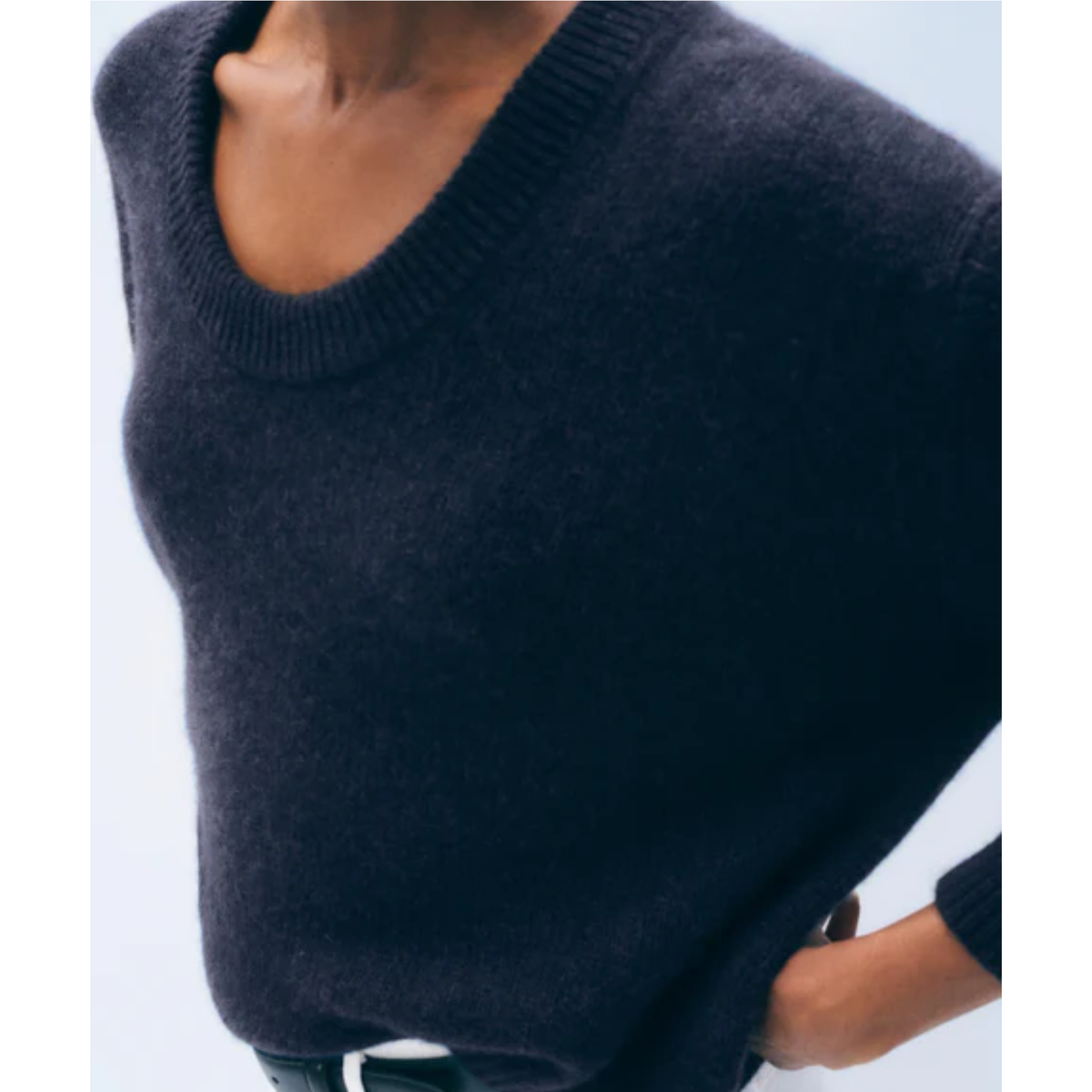 A close-up of a person wearing a dark navy knit sweater with a wide scoop neckline and ribbed trim, paired with a black belt.