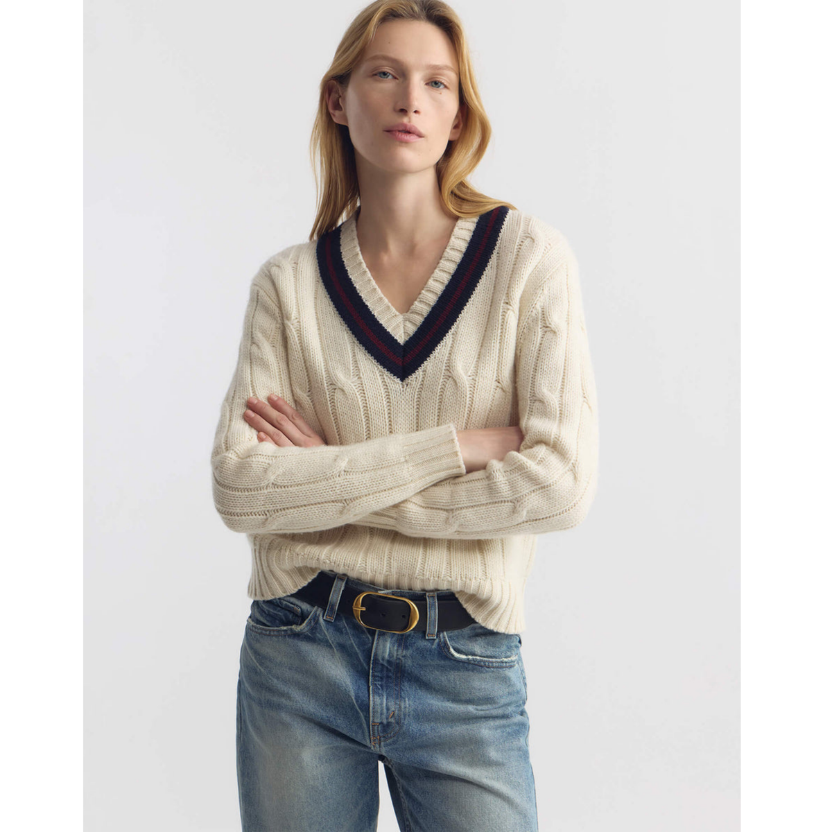 Person wearing a cream sweater with a V-neck and blue collar, paired with blue jeans on a white background.