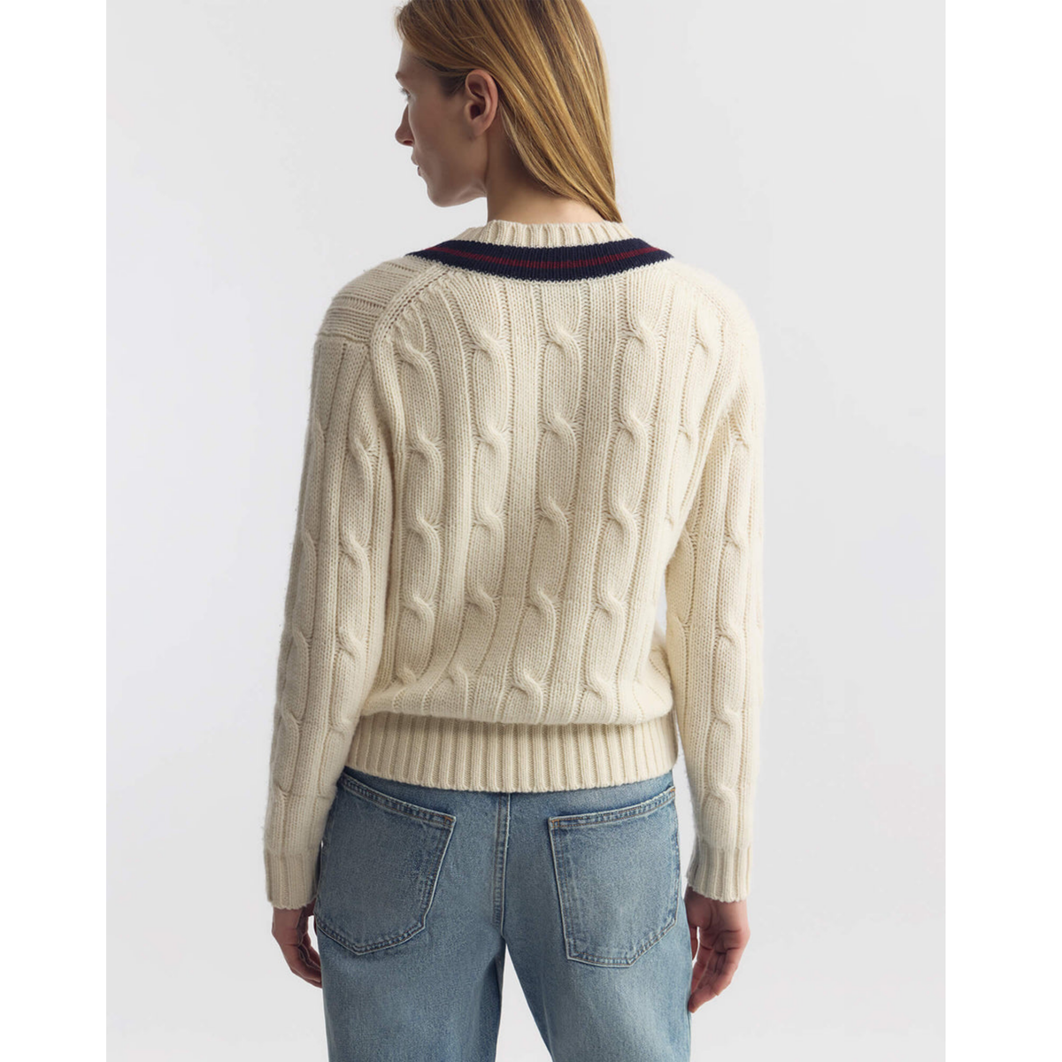 Person wearing a cream cable knit sweater with a navy collar and blue jeans on a white background