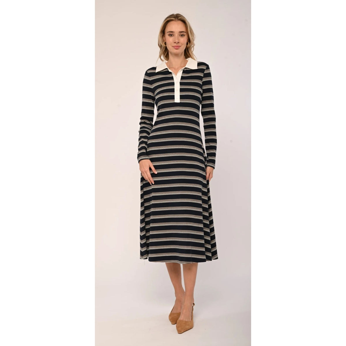 A woman modeling a long-sleeve midi dress with horizontal black and beige stripes, featuring a contrasting cream collar and button placket, paired with tan high heels against a plain light background.