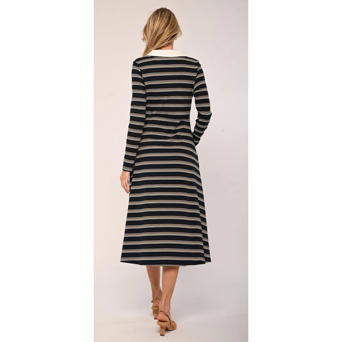 A woman viewed from the back wearing a long-sleeve midi dress with horizontal black and beige stripes, paired with tan high-heeled sandals, against a plain light beige studio background.