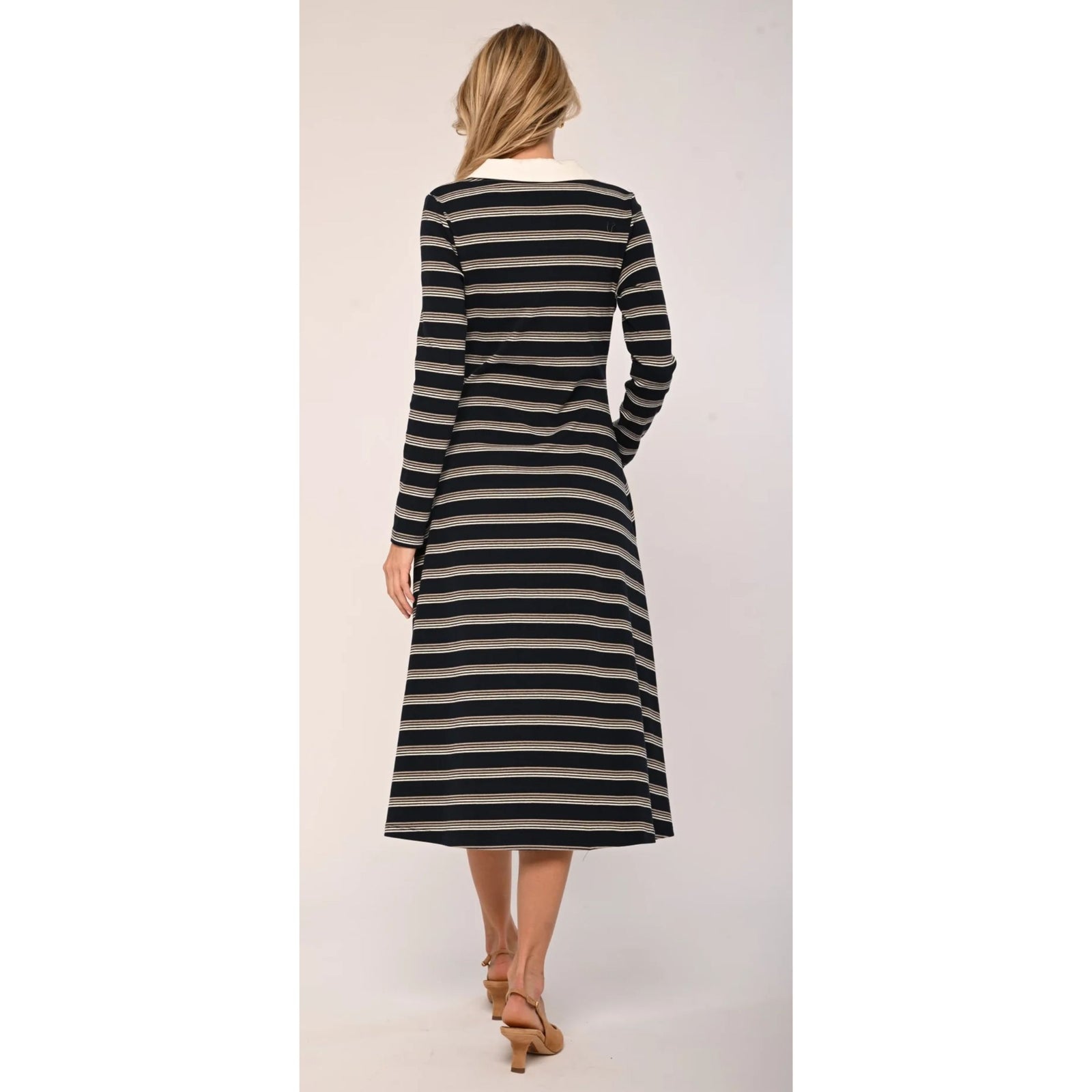 A woman modeling a long-sleeve midi dress with horizontal black and beige stripes, featuring a contrasting cream collar and button placket, paired with tan high heels against a plain light background.