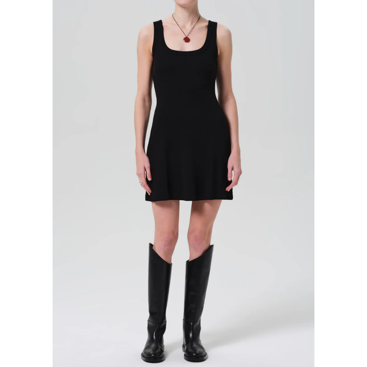Person wearing a black sleeveless dress and black knee-high boots on a white background