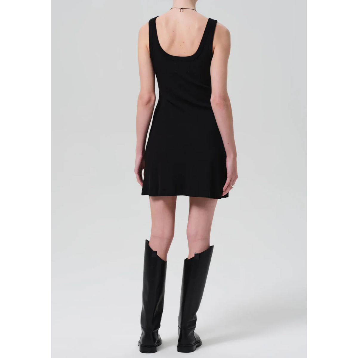 Person wearing a black sleeveless dress and black knee-high boots on a white background