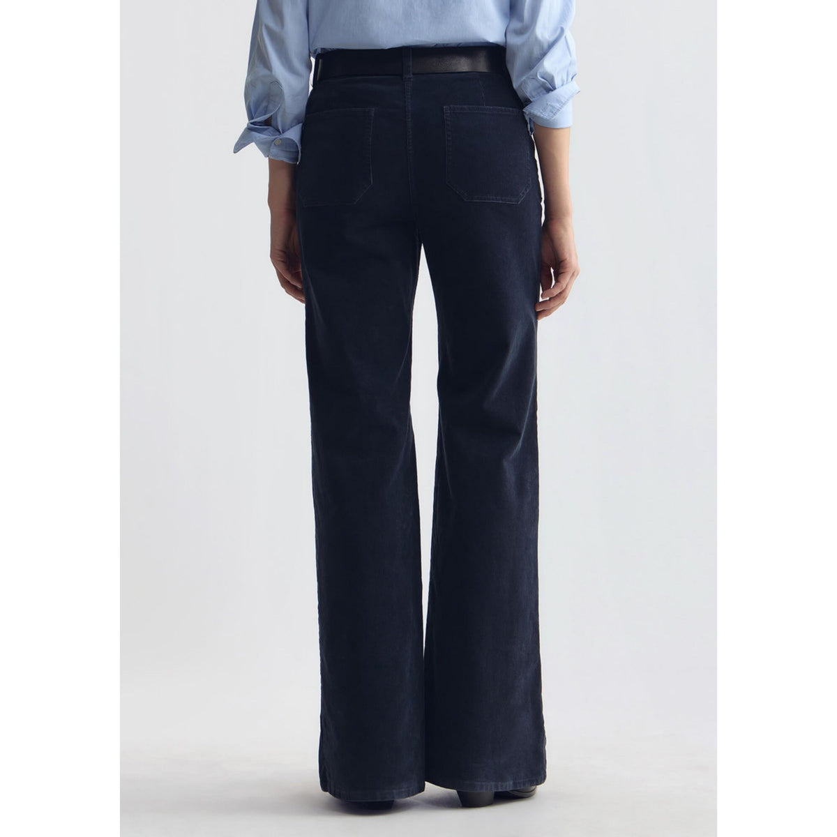 Back view of a model wearing dark navy blue high-waisted wide-leg corduroy pants tucked with a light blue shirt.