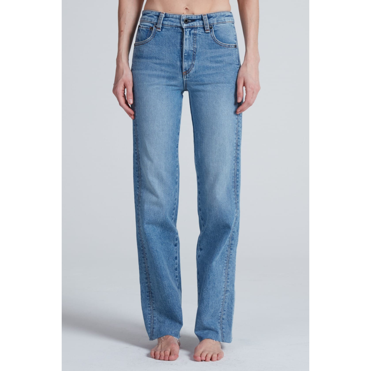 A model wearing a pair of light blue, straight-leg denim jeans, shown from the waist down against a neutral light gray studio background.