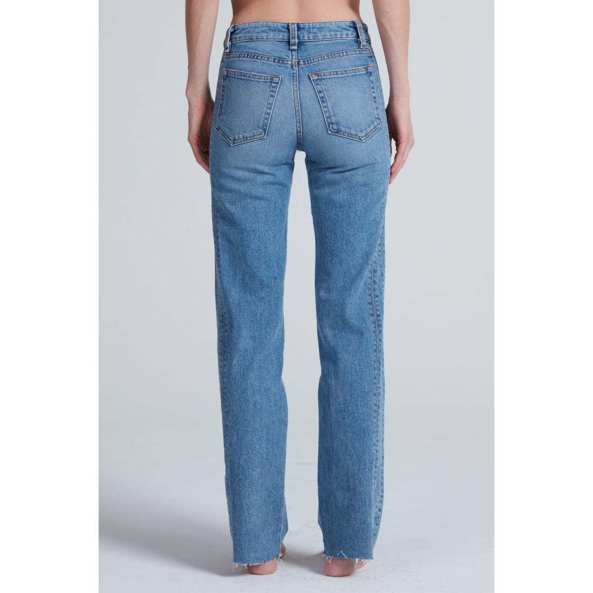 Rear view of a model wearing light blue high-waisted straight-leg jeans with raw frayed hems, shown against a light gray studio background.
