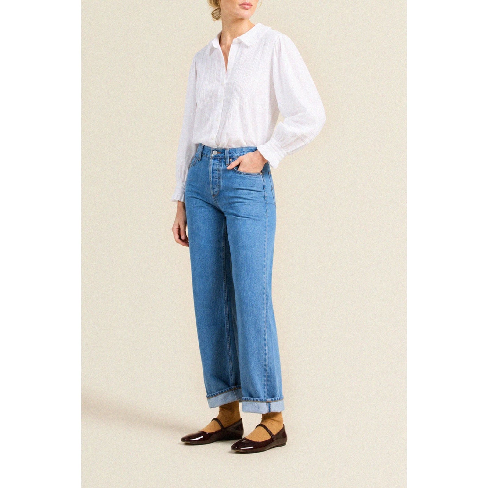 A white long-sleeve button-up blouse with a Peter Pan collar, shown flat against a light beige background.