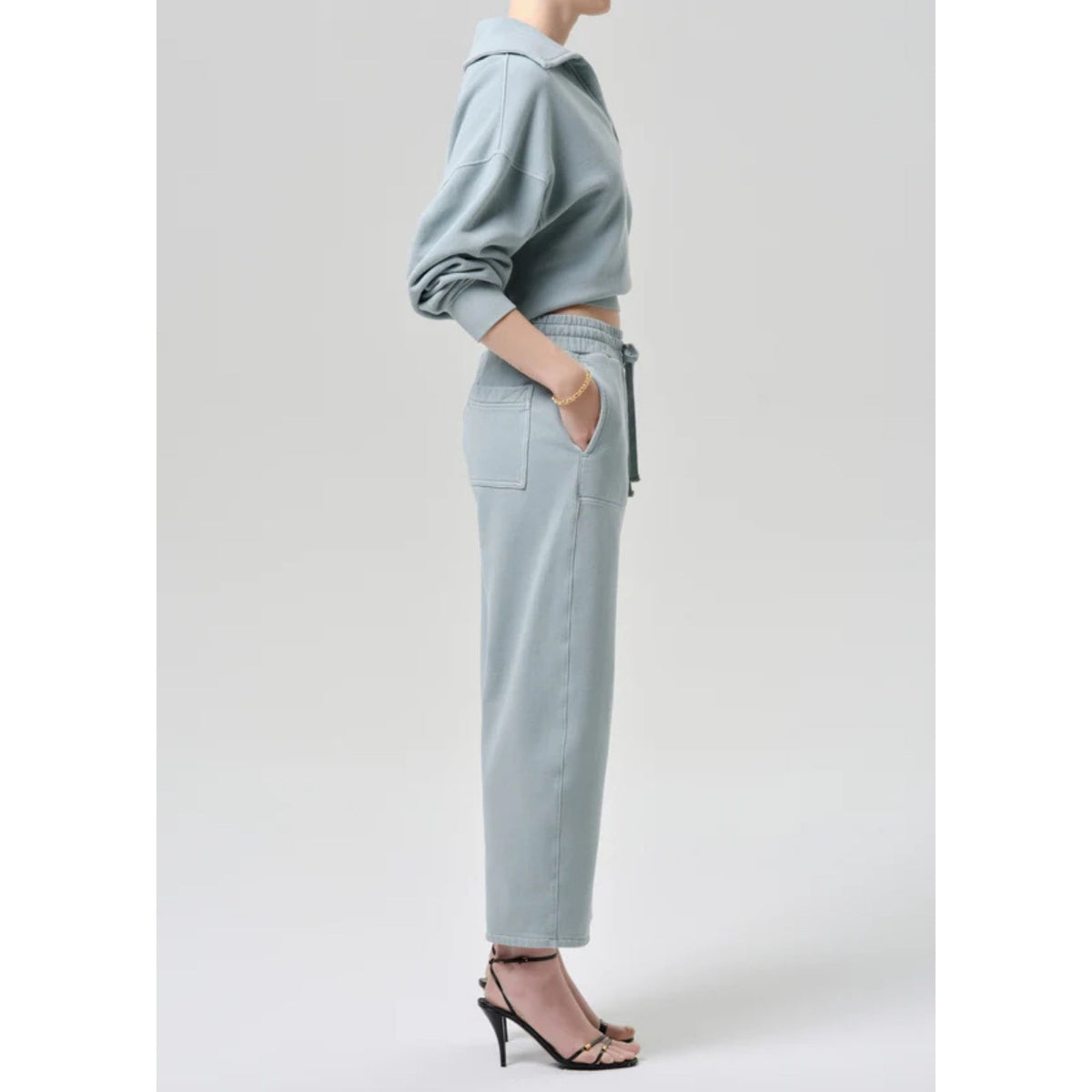 Side profile view from the waist down of a model wearing the light sage green cropped sweatpants with side pockets.