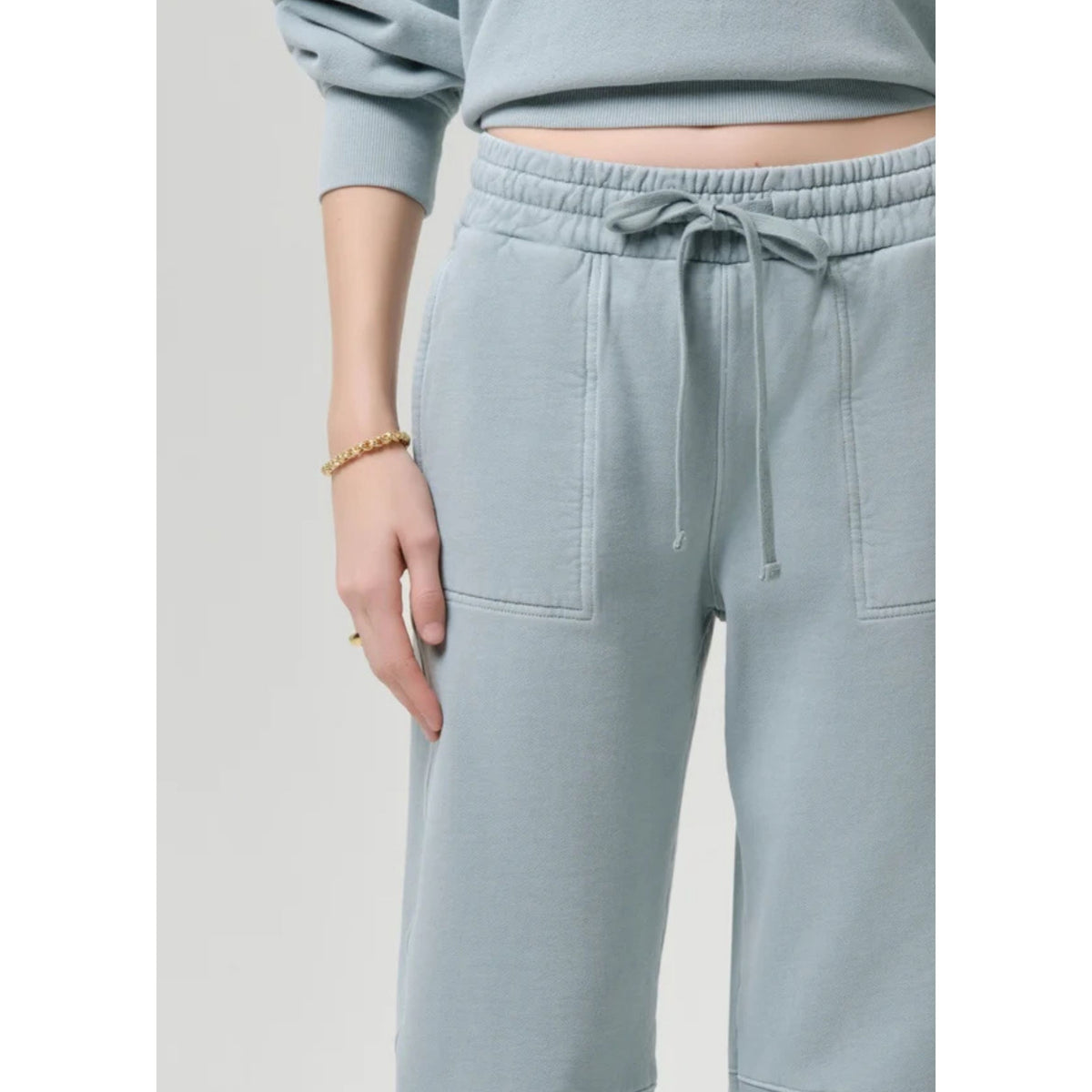Close-up shot of the elastic drawstring waistband, ties, and pocket detail on the light sage green sweatpants.