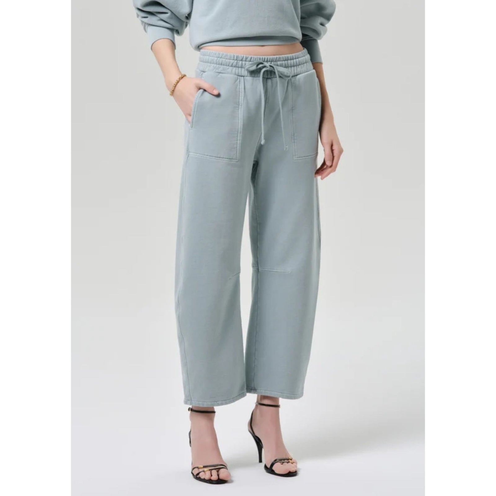Full-length front view of a model wearing the light sage green "Freya Sweatpant" with a drawstring waist, paired with a matching collared long-sleeve sweatshirt and heels.