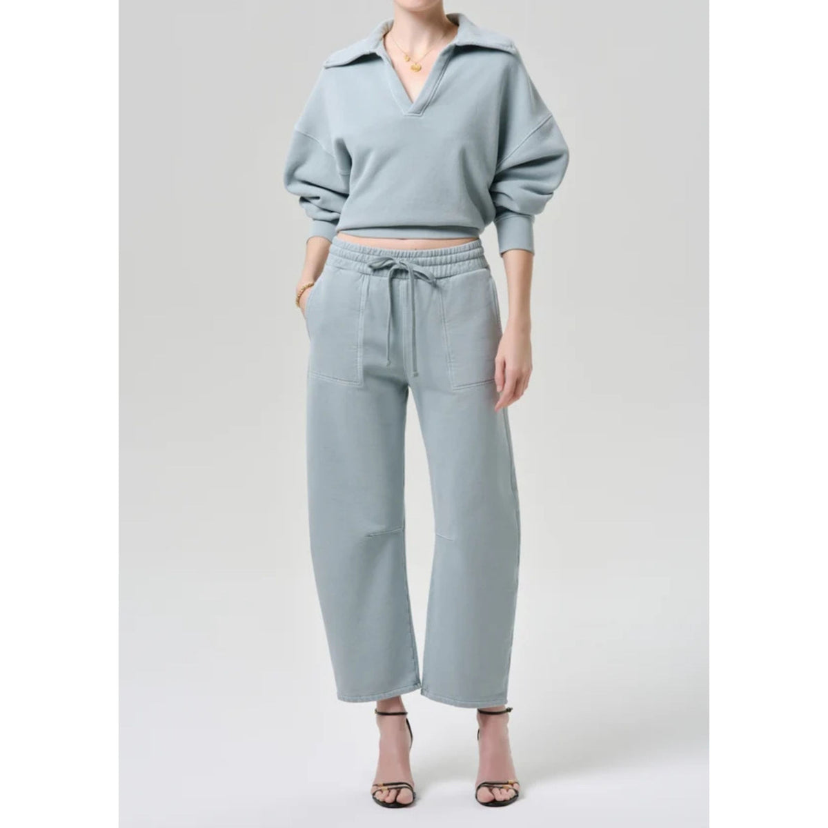 Full-length front view of a model wearing the light sage green "Freya Sweatpant" with a drawstring waist, paired with a matching collared long-sleeve sweatshirt and heels.
