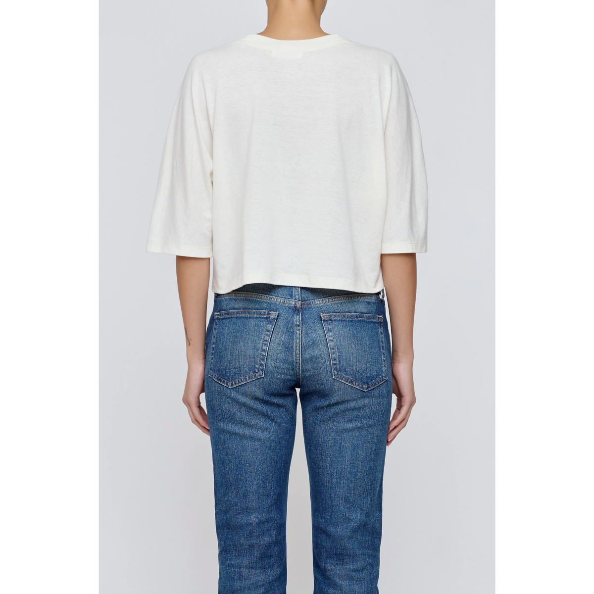 Person wearing a white top and blue jeans on a plain background