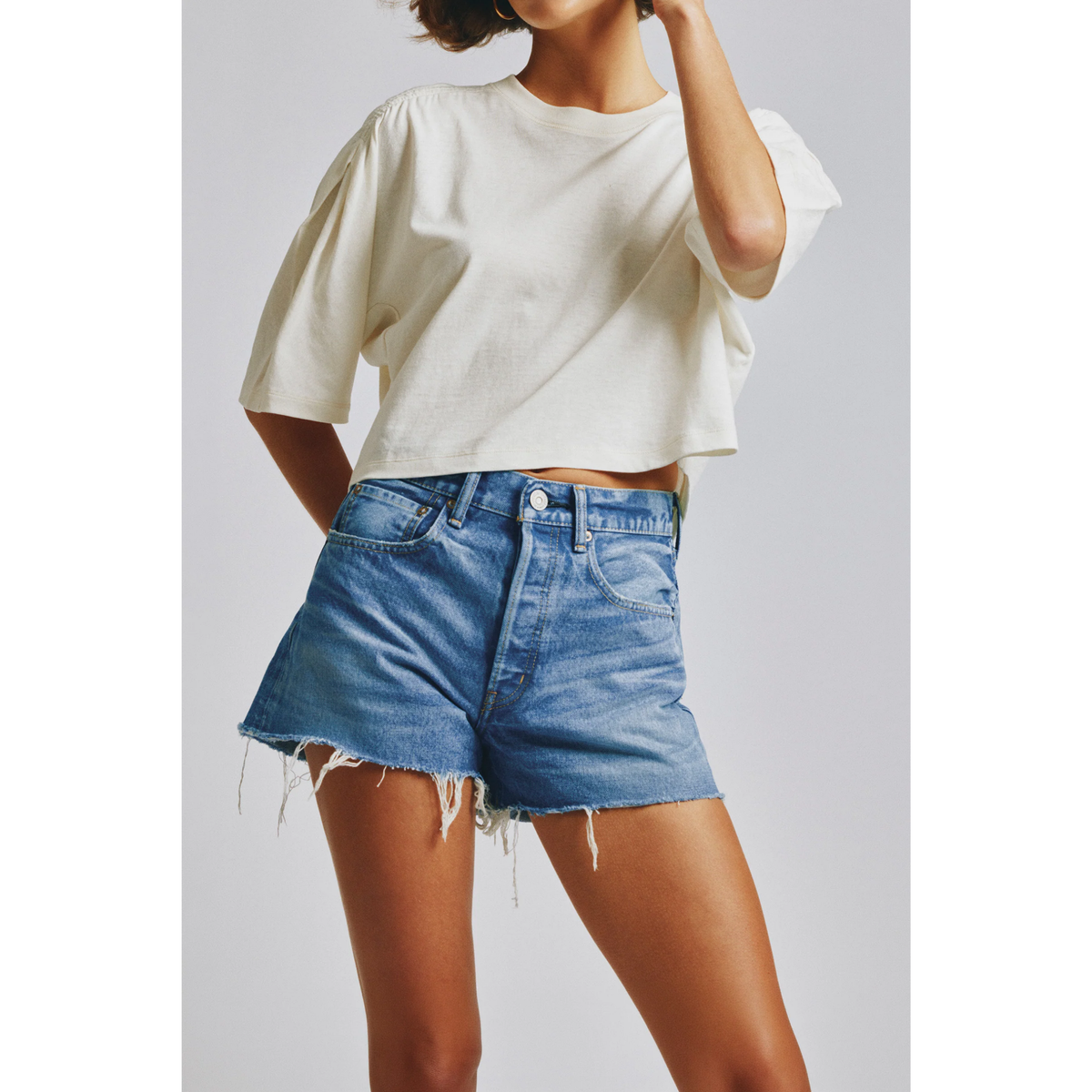 Person wearing a white crop top and blue denim shorts on a plain background