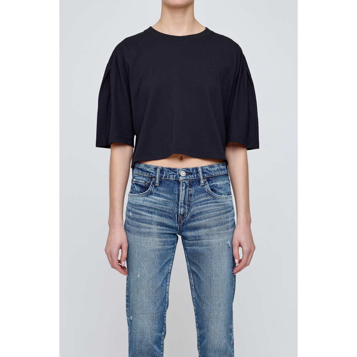 Person wearing a black t-shirt and blue jeans on a gray background