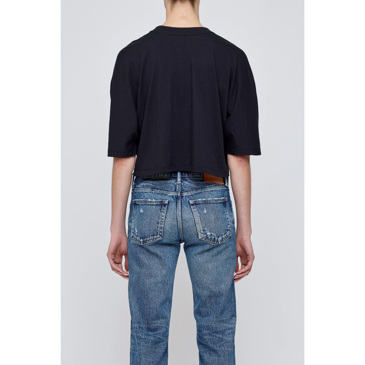 Person wearing a black t-shirt and blue jeans on a plain background