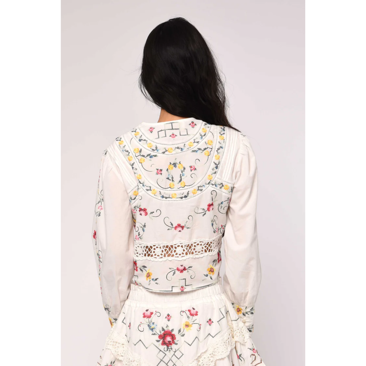 White embroidered blouse with floral patterns on a plain background