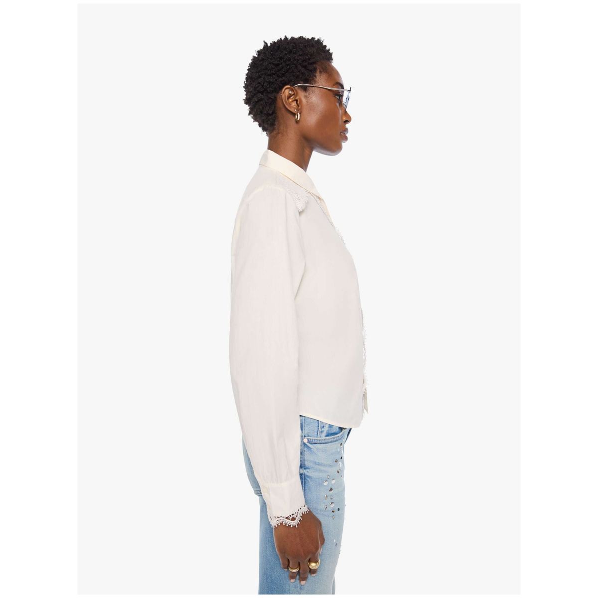 A side-profile view of a model wearing a light cream long-sleeve button-up shirt and light-wash blue jeans against a plain white background.