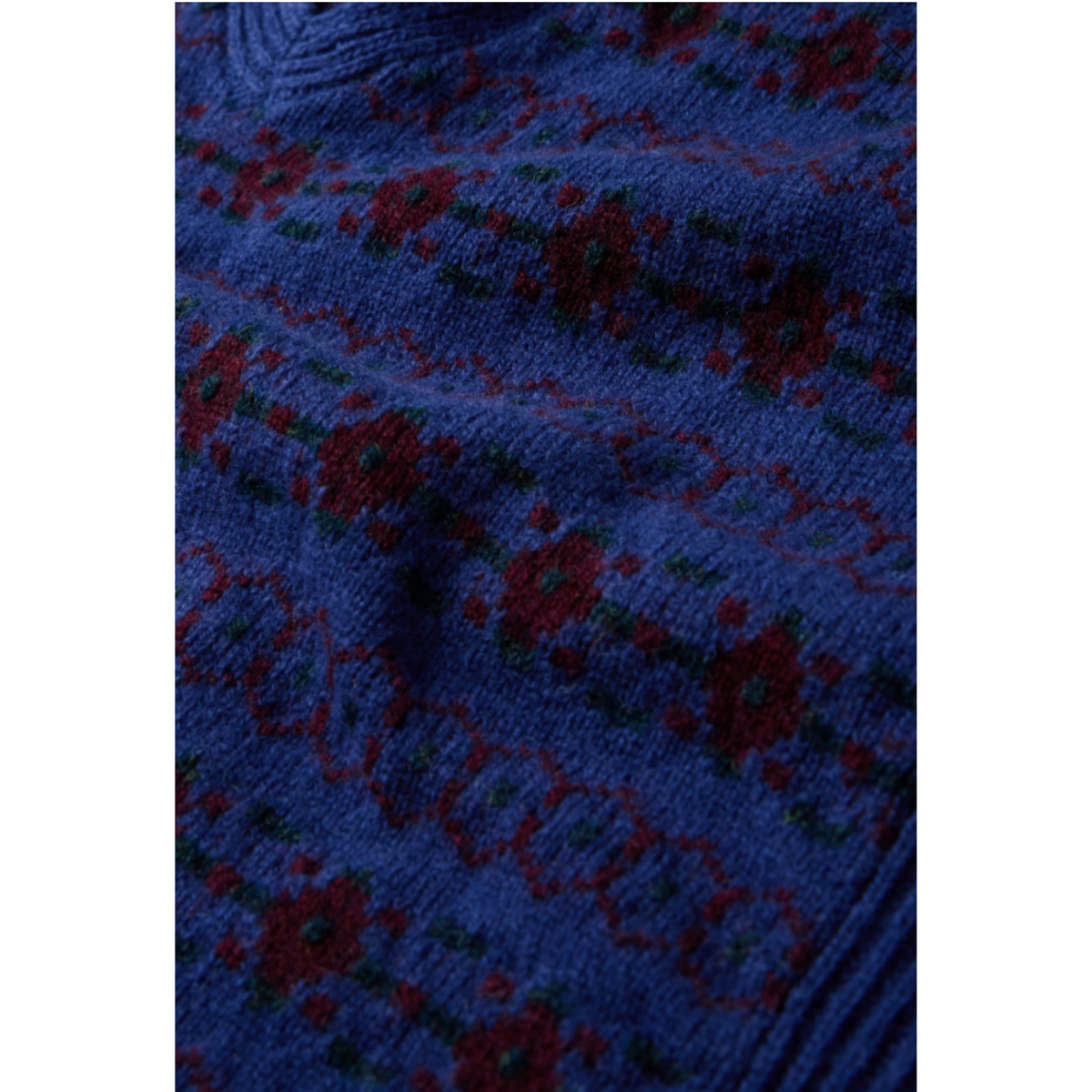 A close-up of a knitted fabric with a blue base and a red and green floral pattern.