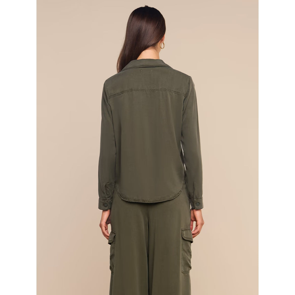 A woman shown from the back wearing an olive green long-sleeve button-up shirt and matching olive green cargo pants against a solid beige background.
