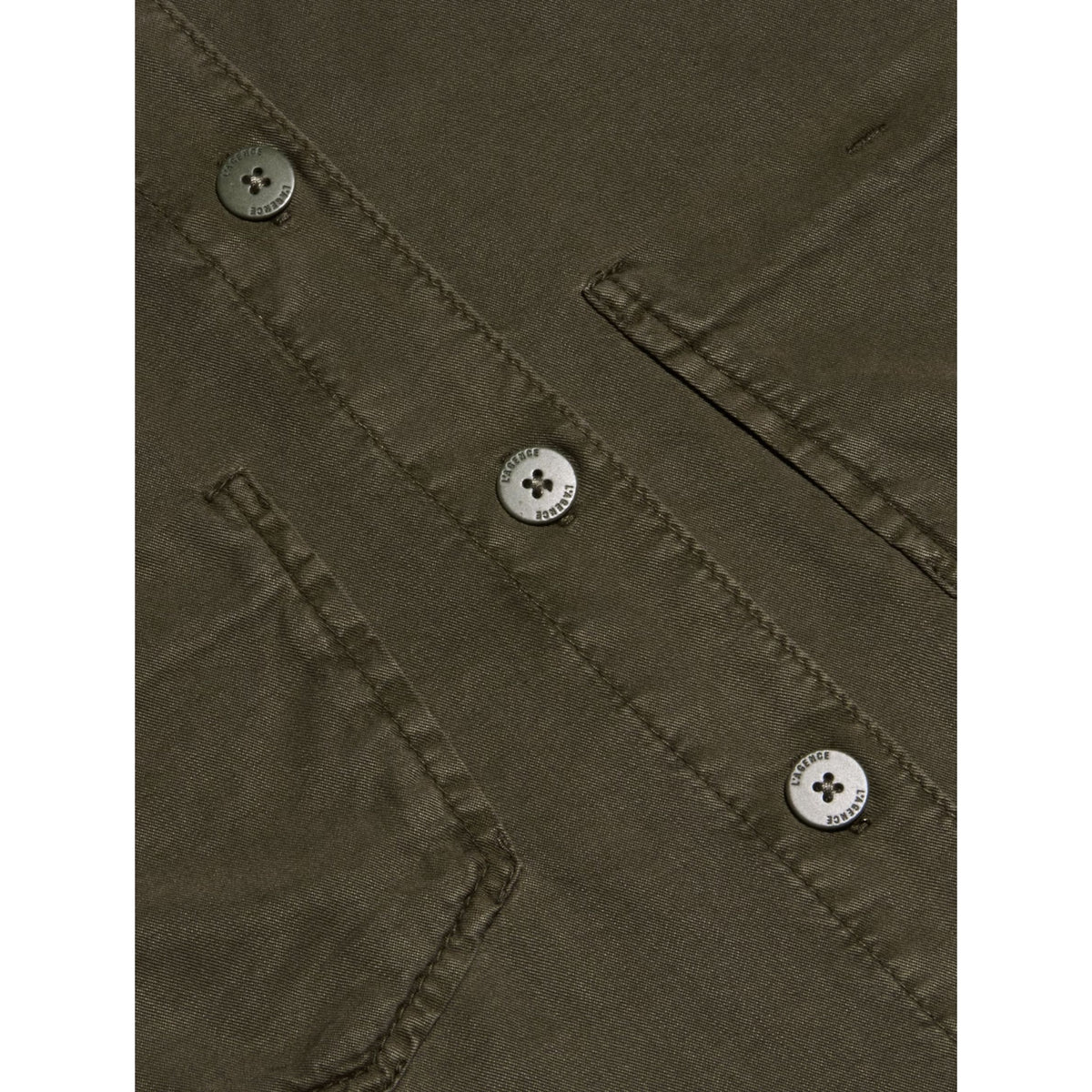 Close-up of an olive green fabric garment showing a buttoned chest pocket and silver-toned buttons.