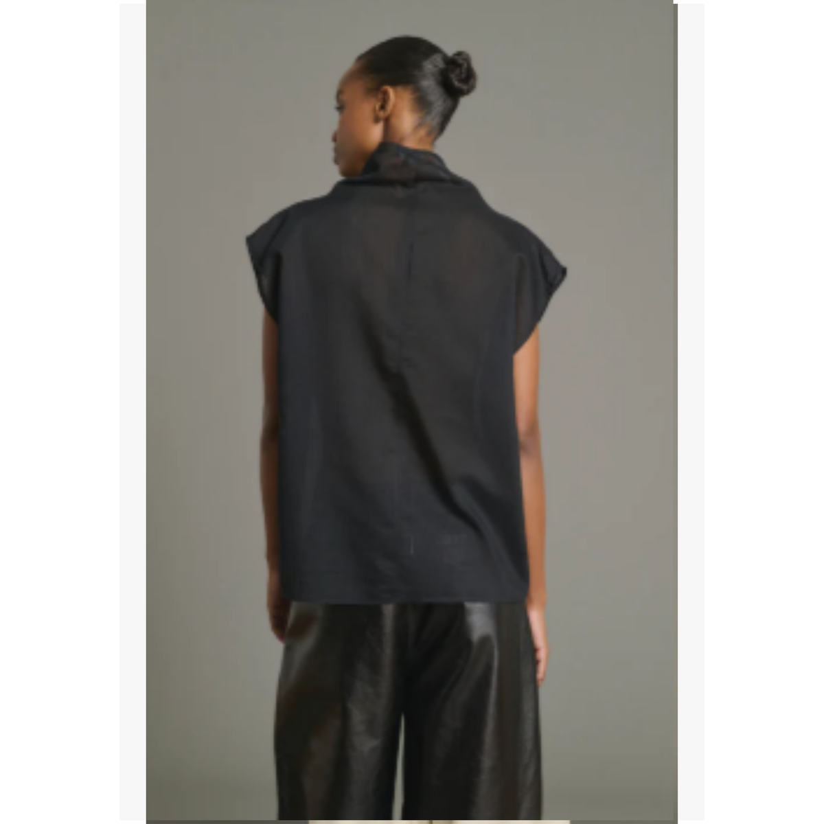 A model shown from the back wearing a black sleeveless collared shirt and black pants against a plain gray studio background.