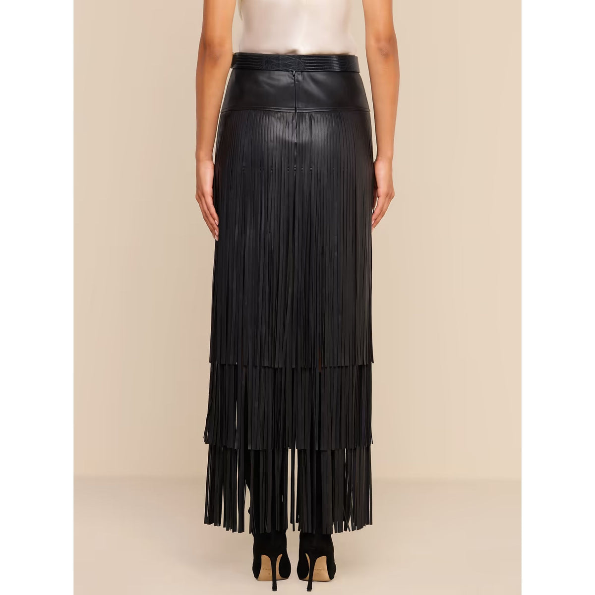 A black faux-leather maxi skirt with a pleated, tiered fringe design, shown on a model from the waist down against a solid beige background.