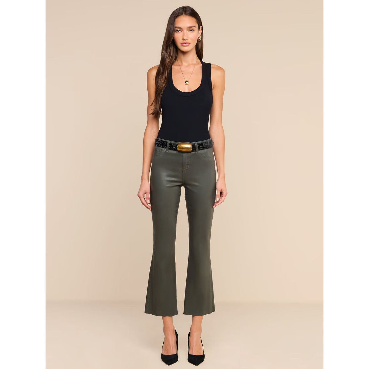 A woman modeling a black sleeveless tank top and olive green cropped flare pants with a black belt, standing against a solid beige studio background.