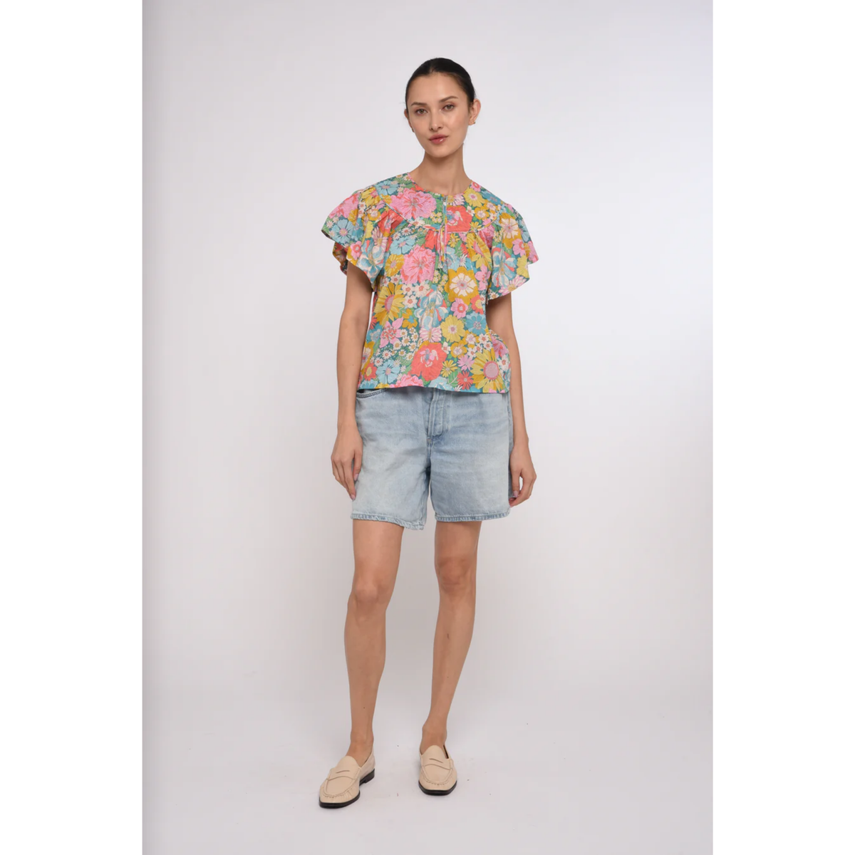 Woman wearing a colorful floral top and denim shorts on a white background
