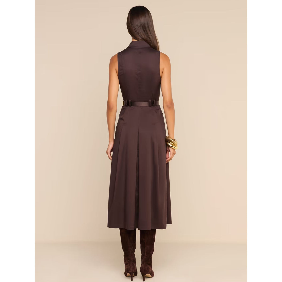 A woman viewed from the back wearing a sleeveless dark brown midi dress with a matching belt and dark brown knee-high boots, standing against a plain beige studio background.