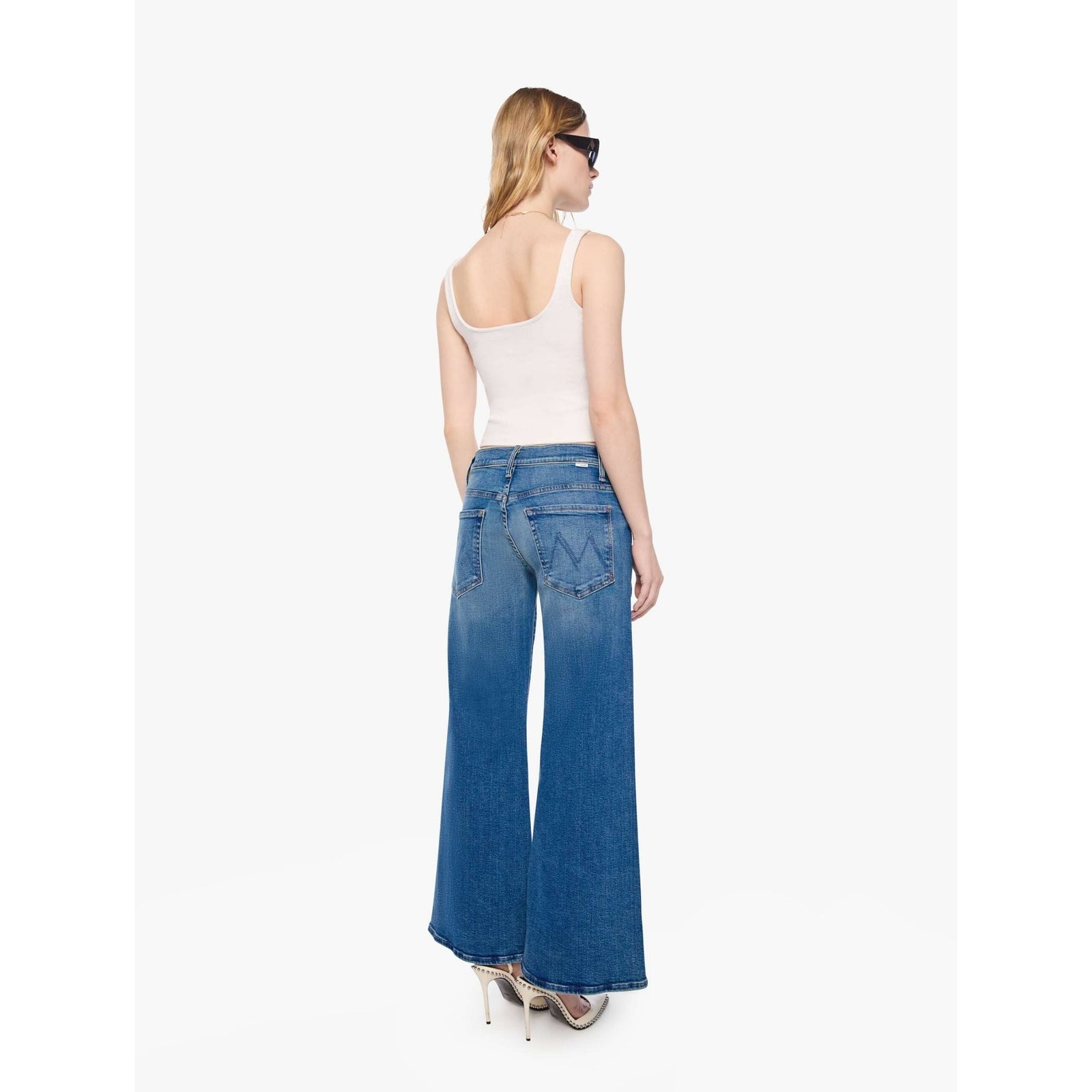 A model wearing blue wide-leg flare jeans, a cream sleeveless crop top, and beige pointed-toe heels, standing against a plain white studio background.
