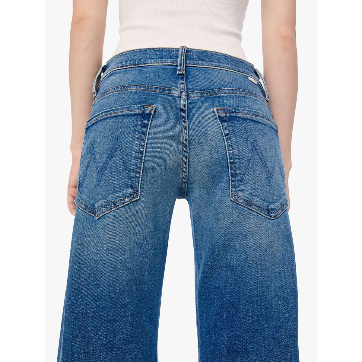 Rear view of a person wearing blue denim jeans with a white top, shown against a plain light background.
