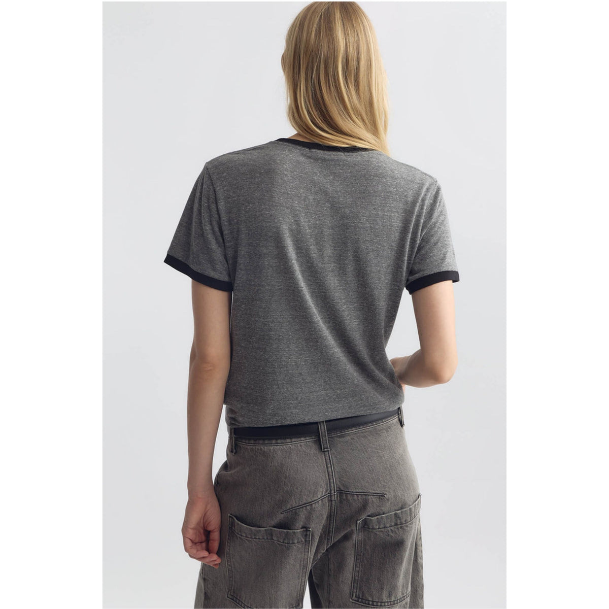 A woman viewed from behind wearing a dark gray heather ringer t-shirt with black trim on the collar and sleeve cuffs, paired with gray jeans.