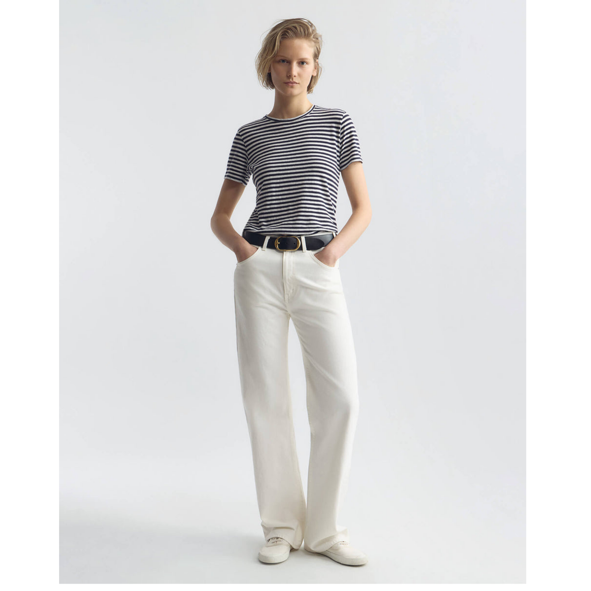 Person wearing a striped shirt and white pants on a plain background