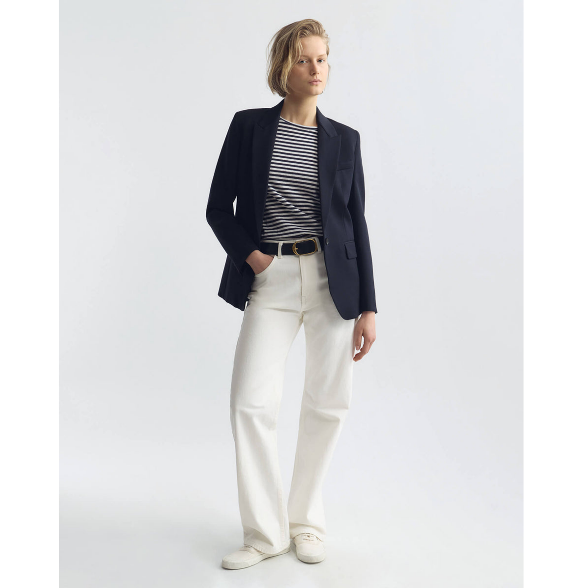 Person wearing a navy blazer, striped shirt, and white pants on a plain background