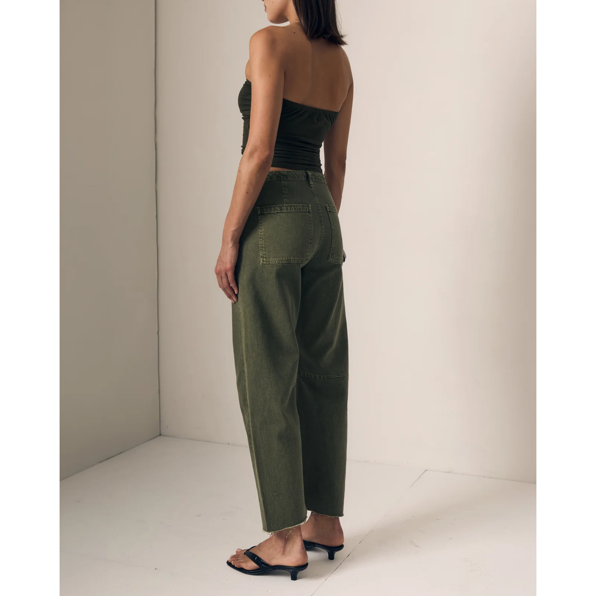 A model shown from the back wearing olive green wide-leg cropped pants, a dark green strapless crop top, and black slide sandals in a minimalist studio setting.