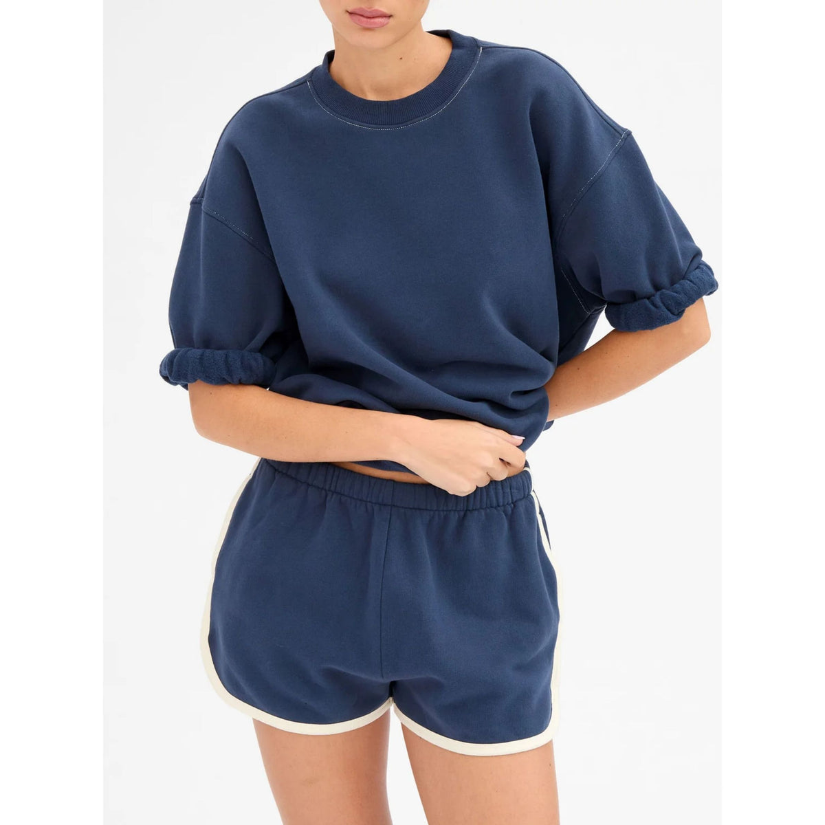 Three-quarter waist-up shot of a model posing in the navy sweat shorts with cream trim and matching short-sleeve sweatshirt with hand on hip.