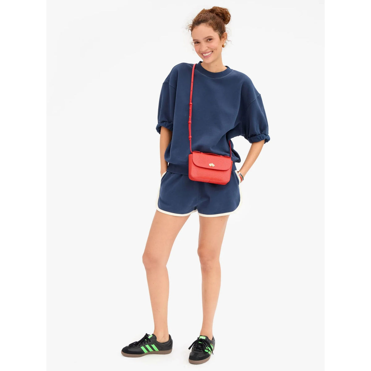 Full-length front view of a model wearing the navy sweat shorts set with white piping, styled with a red crossbody bag and black shoes.