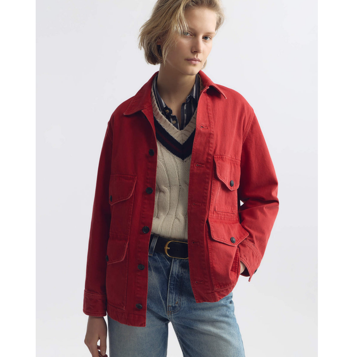 Person wearing a red jacket over a plaid shirt and sweater, standing against a white background
