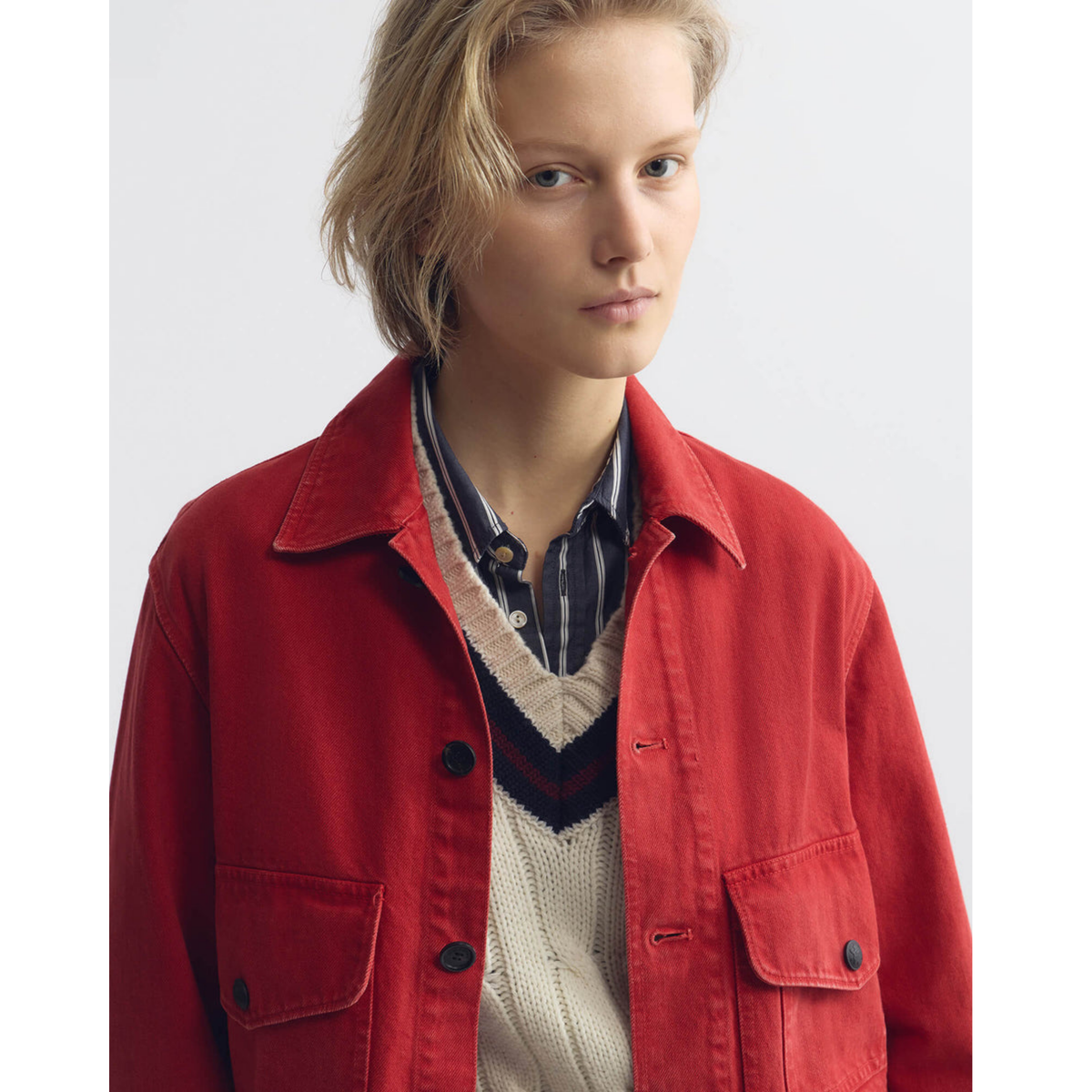 Person wearing a red jacket over a striped shirt and sweater on a white background