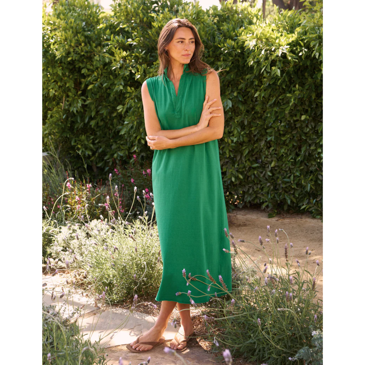 Woman in a green dress standing in a garden with greenery and flowers around her.