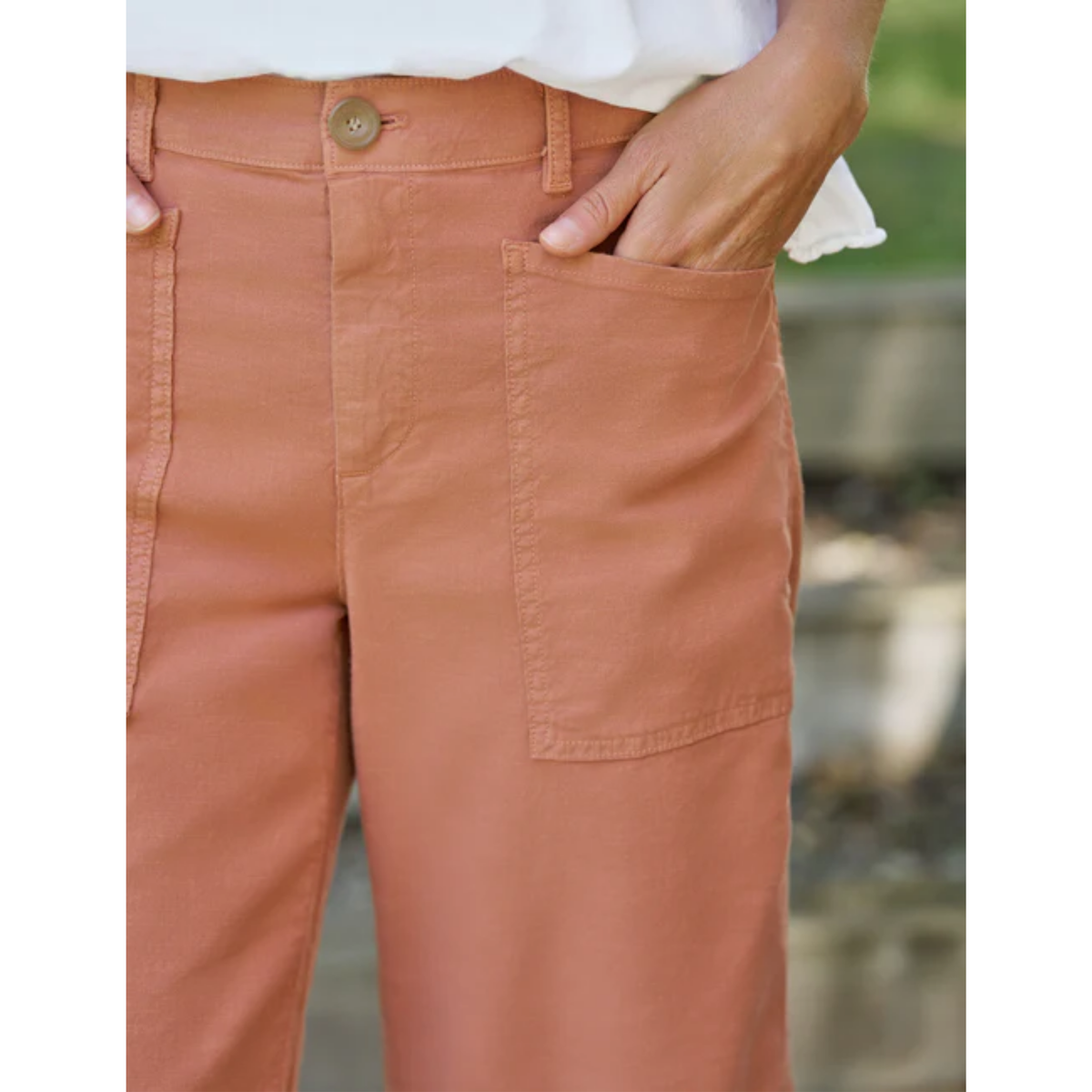 Close-up of a person wearing terracotta-colored pants with a white top, showing the front pocket and hand in the pocket.