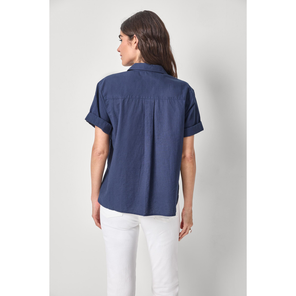 Woman wearing a navy blue shirt and white pants on a light gray background