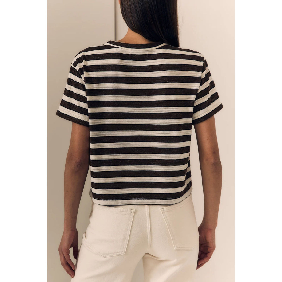 A woman shown from the back wearing a short-sleeve striped crop top with black and off-white horizontal stripes, paired with off-white pants.