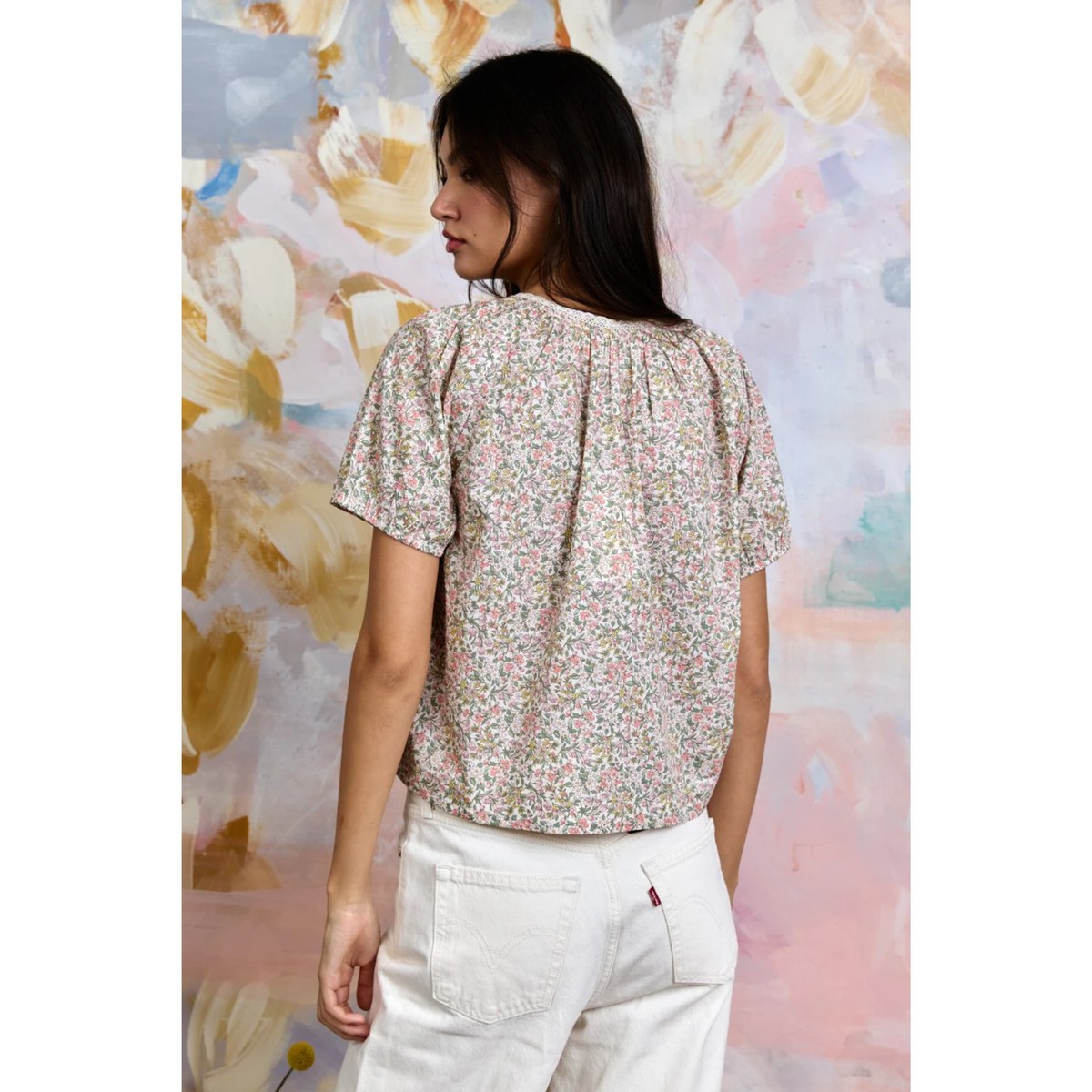 Woman wearing a floral blouse and white pants against a colorful abstract background
