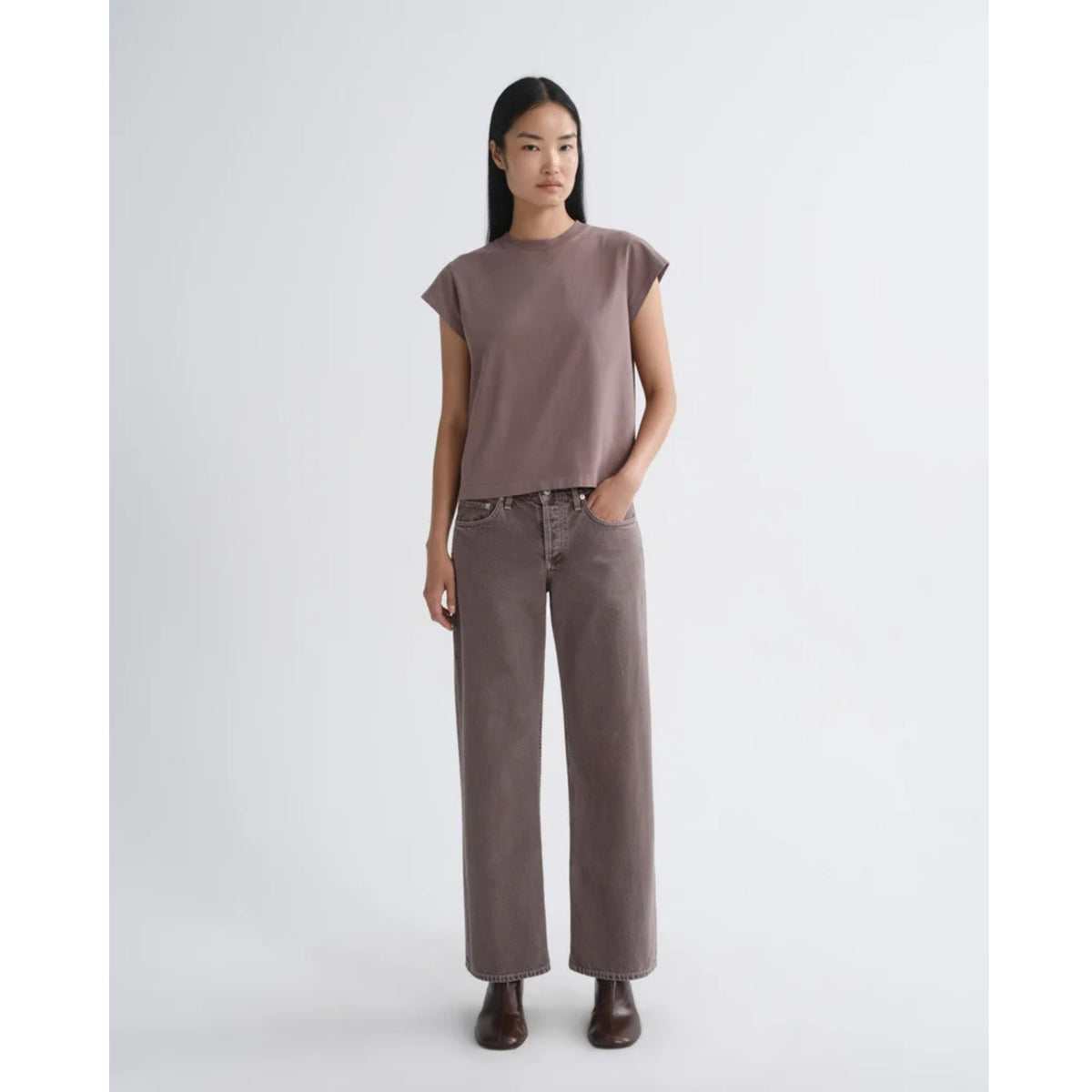 Full-length front view of a model wearing a short-sleeve dusty mauve top and AGOLDE Low Rise Loose jeans with dark boots against a light gray background.