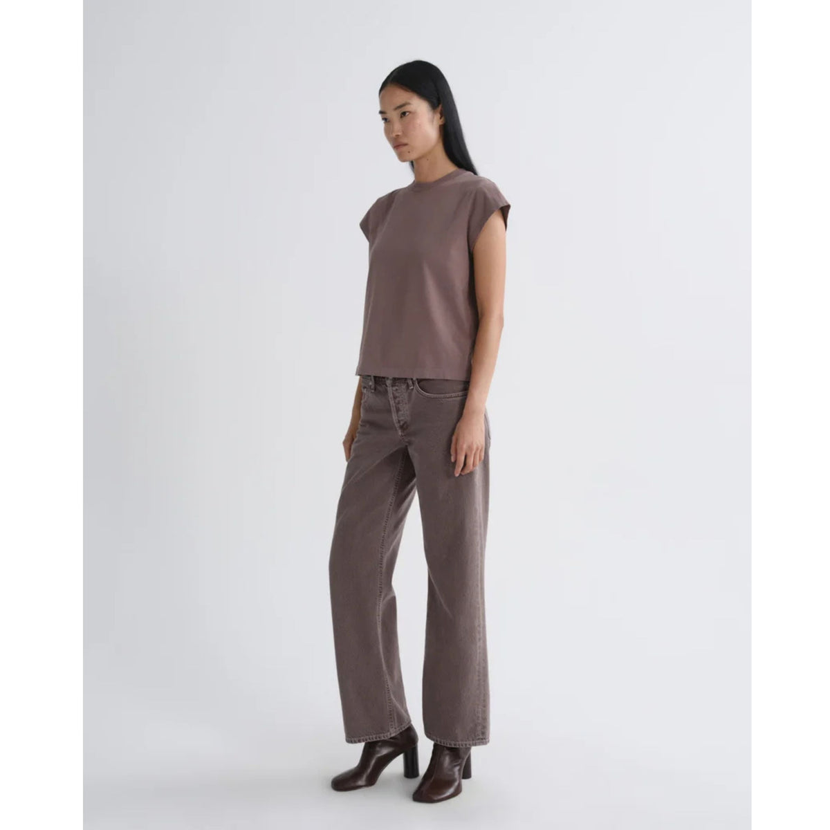 Full-length front view of a model wearing a short-sleeve dusty mauve top and AGOLDE Low Rise Loose jeans with dark boots against a light gray background.