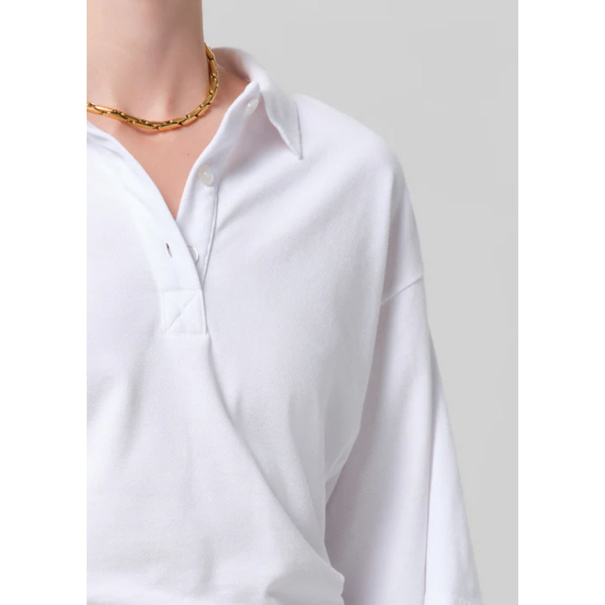 White shirt worn by a person with a gold necklace on a plain background