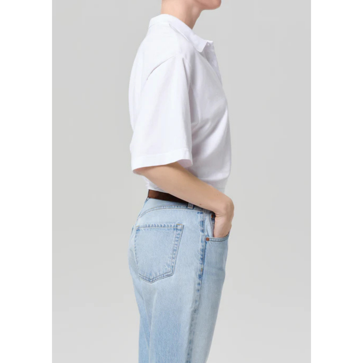 Person wearing a white shirt and light blue jeans on a plain background